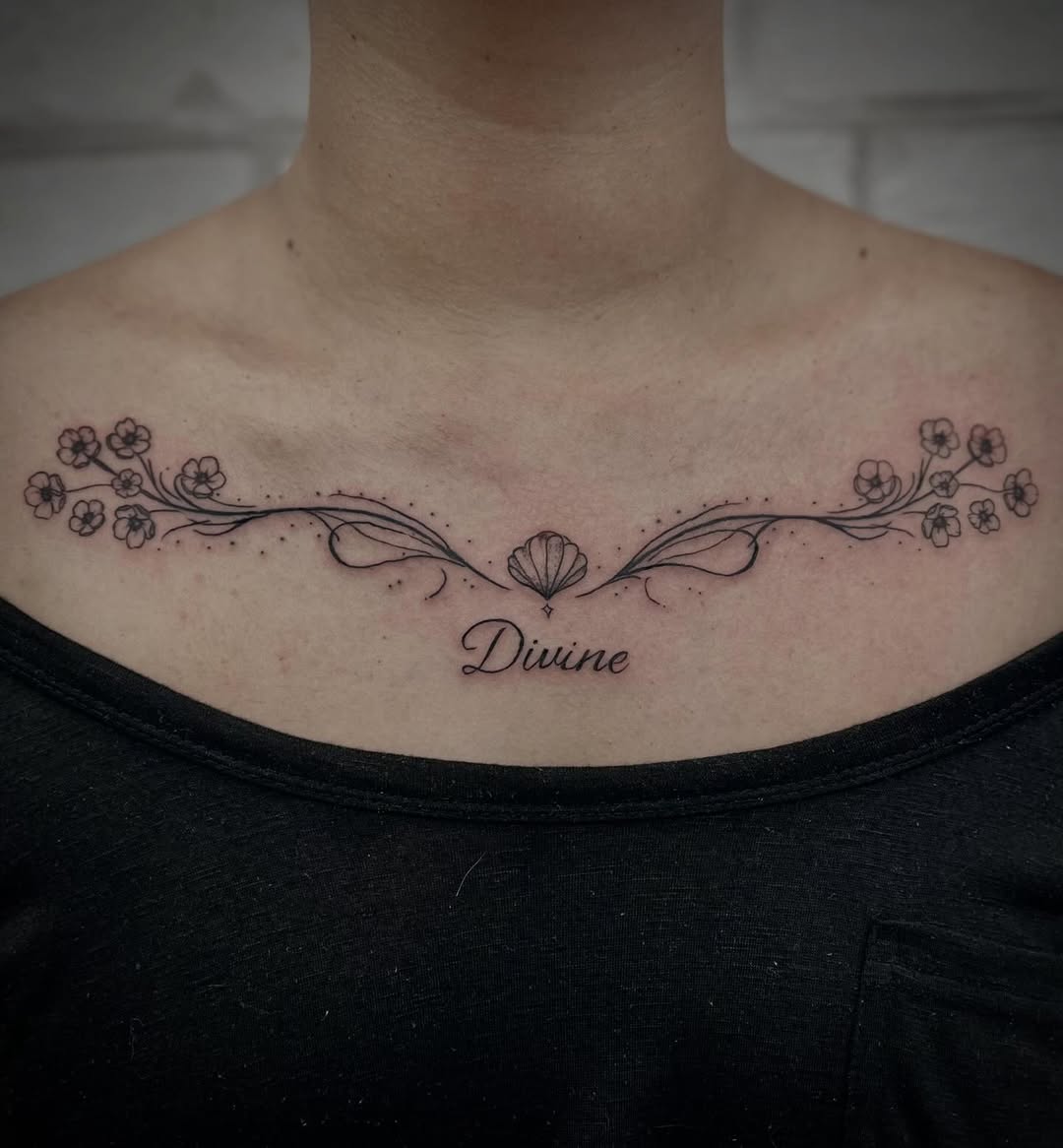 Tatuagem floral de linhas finas sobre o peito, com texto por baixo