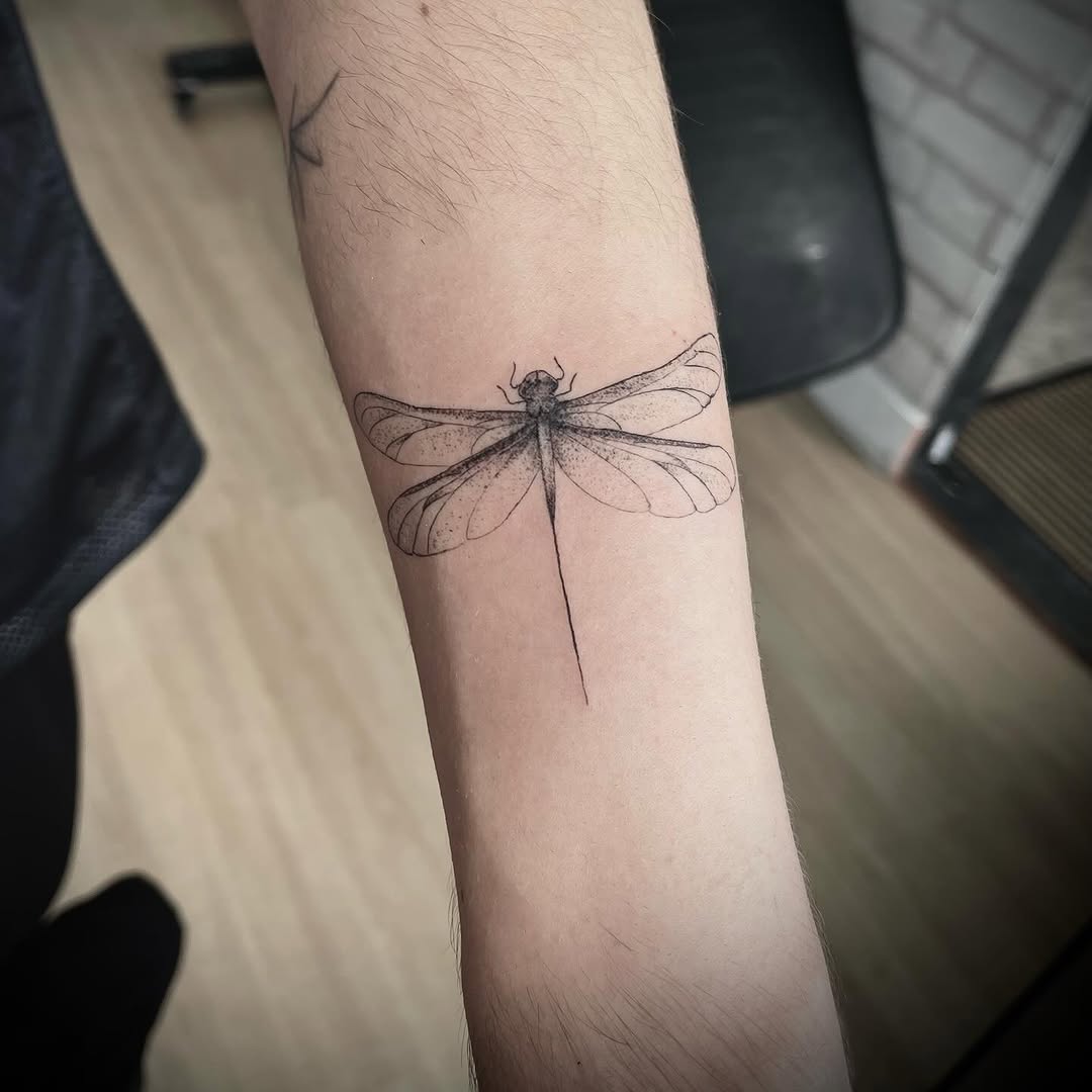 Tatuagem de libélula no antebraço, em traço fino